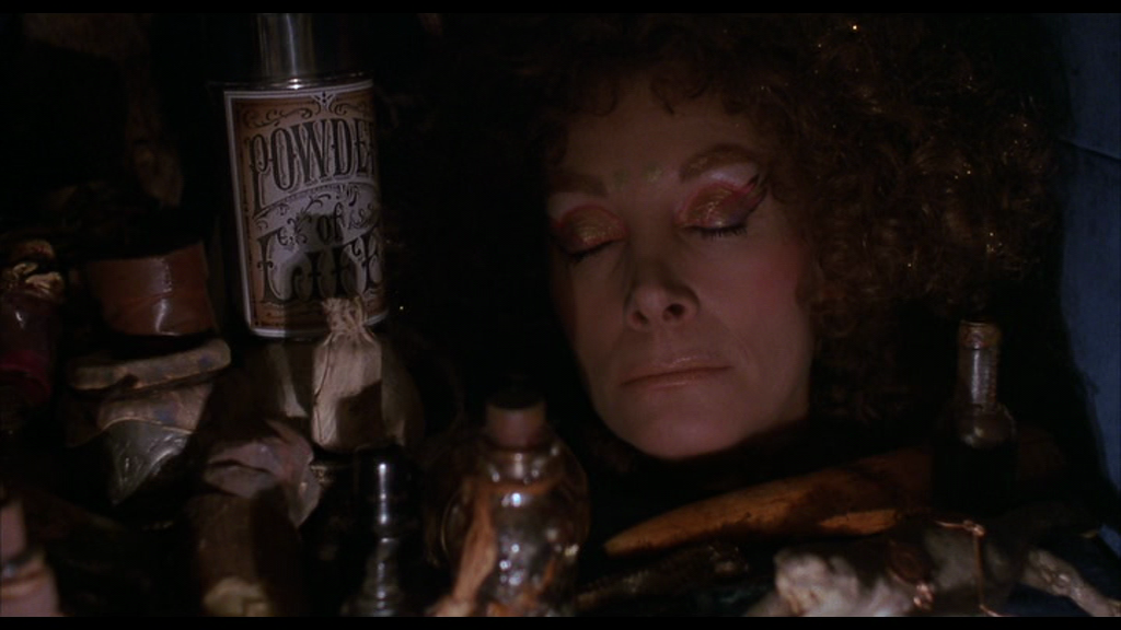 An image from the film Return to Oz featuring Jean Marsh's Mombi with her eyes closed in a tight space. She's only a head and is surrounded by bottles of potions, including the Powder of Life.