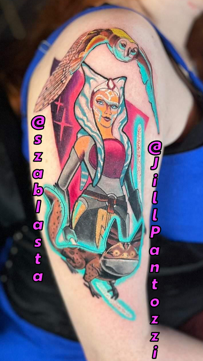 It's my right arm facing outward featuring my new Ahsoka Tano tattoo. It's done in bright blues, pinks, and more and sees Morai on the very top of my shoulder followed by Ahsoka with her lightsabers, and finally a lothcat at the very bottom. All figures are alight from the glow of the sabers.